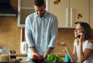 Attractive couple in the kitchen early morning. Beautiful girl chatting phone while her boyfriend cooking breakfast at home